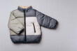 Fashion baby colorblock puffer jacket on grey background. Top view, flat lay. Newborn beige clothes outfit. Winter, autumn collection. Template with copyspace for brand, logo, advertising. Banner