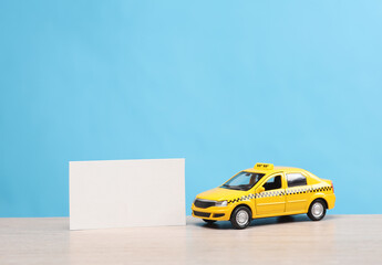 Wall Mural - Miniature taxi car with a white business card on table, blue background