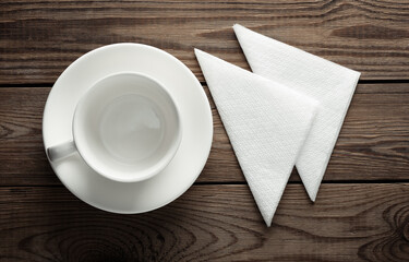 Wall Mural - Empty white ceramic cup with saucer and napkins top view on wooden table