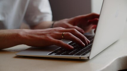 A programmer writes code for a website. A man with a ring on his finger works on his laptop while sitting in a cafe.