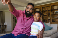 Happy African American Father And Son Sitting Embracing And Pointing Away