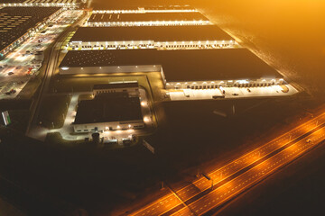 Wall Mural - Many warehouses in an industrial area, aerial view of brightly lit logistics warehouses at night, trading business