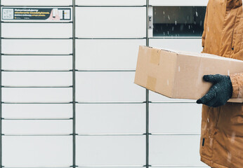 Wall Mural - A man with a box in his hands near the self-service mail terminal. Parcel delivery machine. Person holding a cardboard box. Mail delivery and post service, online shopping, e commerce concept