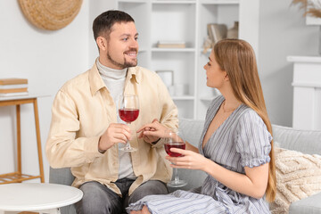 Sticker - Young couple with glasses of wine sitting on sofa at home