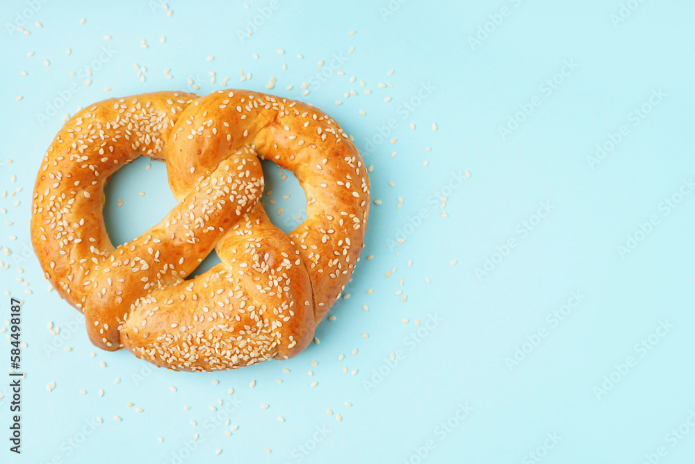 Tasty pretzel with sesame seeds on color background