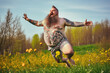 canvas print picture - Glücklicher, übergewichtiger Mann mit Tattoos und langem Bart macht einen Luftsprung auf einer Wiese - Generative AI