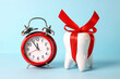 White tooth model with red bow ribbon and alarm clock on a blue background.