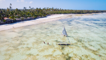 Take in the stunning scenery of Zanzibar's tropical coast from above, as fishing boats rest on the sandy beach at sunrise. The view from the top reveals clear blue waters, green palm trees, and even 