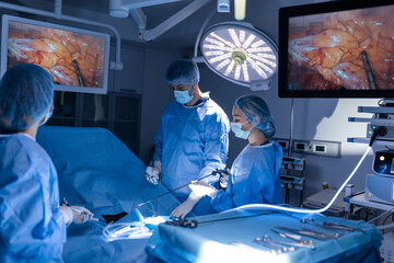 Wall Mural - Three surgeons doing laparoscopic surgery. Doctors looking at image on monitor. Medicine and healthcare concept. Internal organ of patient seen on computer monitor