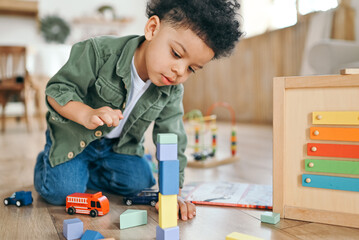 Concentrated latinos boy playing toys sitting on warm floor in modern living room. Baby development. Small tower. Learning creative concept