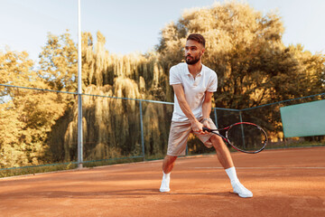 Wall Mural - Active training. Young man is on the tennis court at sunny daytime