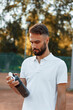 © standret - Drinking water, taking a break. Young man is on the tennis court at sunny daytime