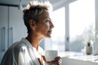 © nenetus - Attractive mature woman looking forwards while drinking a coffee in the living room at home. Generative AI