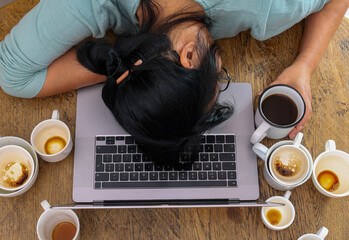 Exhausted female worker surrounded by coffee cups sleeping at workplace over laptop. Tired over work woman having too much work and coffee, napping on laptop. Caffeine addicted bad lifestyle concept.