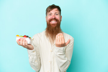 Wall Mural - Redhead man with long beard holding a bowl of fruit isolated on blue background inviting to come with hand. Happy that you came