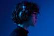 © SHOTPRIME STUDIO - Teenage man wearing headphones listening to music and dancing and singing open mouth with glasses, hipster lifestyle, portrait blue background, neon light, style and trends, mixed light, copy space