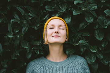 Portrait of relaxed and confident woman with eyes closed on background of green leaves wall. Thoughtful person in front of green hedge. Joy, zen and balance people. Stability through mental health