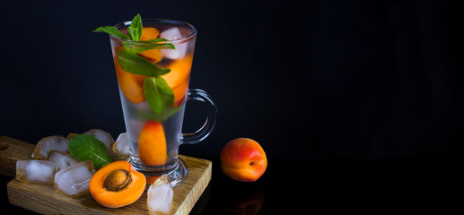 Wall Mural - Infused or detox water with apricot and mint in the drinking glass on the dark  background. Close-up. Copy space.