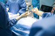 Man in operating room passing surgical instrument to colleague
