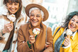 Three mature women eating ice cream cone outside - Older female friends having fun walking on city street - Joyful elderly lifestyle concept