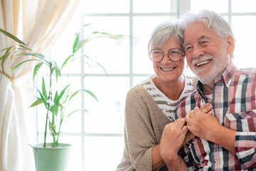 Wall Mural - Happy senior couple embracing and laughing sitting at home. Modern retirees laugh at something funny, expressing happiness and carefree