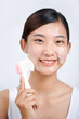 © Marc Tran/Stocksy - Young woman using facial cleansing brush on white background.
