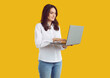© Studio Romantic - Young businesswoman using laptop computer. Portrait of young business woman in white shirt standing isolated on yellow background, holding notebook computer and looking for information on the Internet