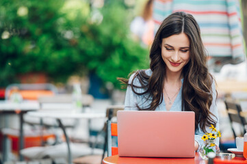 Beautiful woman sitting in a street cafe and using a laptop