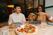 © Jimena Roquero/Stocksy - Friends sharing pizza in restaurant having fun. UGC
