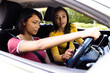 © Wavebreak Media - Happy biracial sisters sitting in car talking, one sister giving the other a driving lesson
