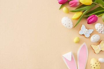 Wall Mural - Easter decor idea. Top view composition of easter bunny ears colorful eggs yellow pink tulips and butterfly cookie on isolated beige background with copyspace