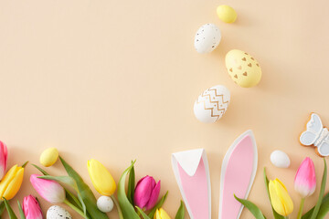 Wall Mural - Easter celebration concept. Flat lay composition of easter bunny ears colorful eggs yellow pink tulips and butterfly cookie on pastel beige background with copy space