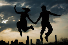 Happy Couple Jumping Against A Cityscape And Sky Background