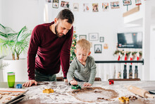 A father and toddler son cut out gingerbread cookies together