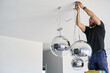 © Rowena Naylor/Stocksy - Electrician hanging large globe mirror lights
