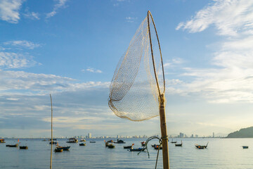 Wall Mural - A hoop net sticking against a blue sky with fishing boats on a harbour at Da Nang Vietnam