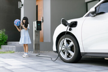 A playful and happy girl playing around at her home charging station providing a sustainable power source for electric vehicles. Alternative energy for progressive lifestyle.