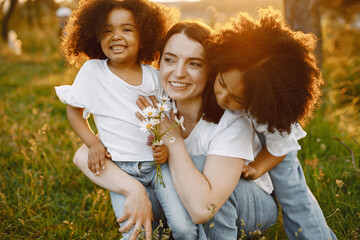 Caucasian mother embracing her two mixed race daughters in a sunset