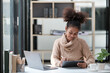 © Treerat - American African Woman working in the office with computer phone and Tablet.