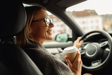 Smiling Businesswoman Wearing Eyeglasses Sitting Behind Steering Wheel In Car And Drinking Coffee 