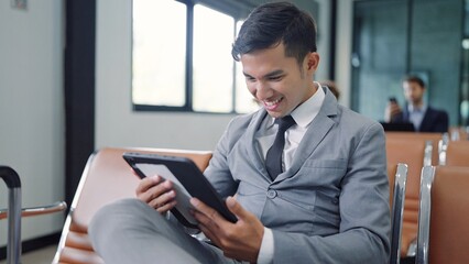 Smiling face of happy Asian businessman sitting and working on laptop waiting for flight at airport terminal