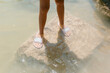 © Jimena Roquero/Stocksy - Child's legs standing on rock inside pond