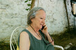 © Jimena Roquero/Stocksy - Grey-haired woman in countryside house garden speaking on smartphone