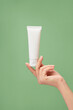 © Tuan  Nguyen  - Over a pastel green background, woman hand model holding a white tube without label. Beauty product mockup. Natural skincare products concept