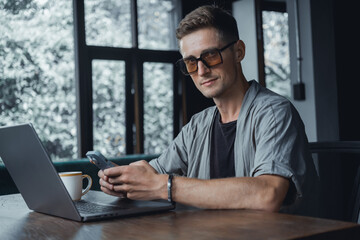 Young man using smartphone in hand, office,happy face, outdoor hipster portrait on the cafe, smile happy face, listen music on headphones, Amsterdam street, dance, player,photo concept, laptop