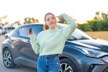 Canvas Print - Young pretty girl holding car keys at outdoors having doubts and with confuse face expression