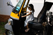 © Anton - Caucasian girl with dark hair in a white dress poses behind the wheel of an Indian motorized rickshaw. Tourism in Asia. Children's adventures in India.Playing as a motorized rickshaw driver.Incredible