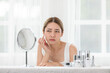© 220 Selfmade studio - Asian young woman looking in mirror worry about pores facial skin problem with acne and dry skin. Self care and Skin care concept