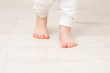 © fotoduets - Little child legs in white trousers on light wooden floor background. Barefoot closeup. Front view.