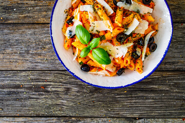 Noodles with pesto, parmesan cheese, basil and black olives served on wooden table
